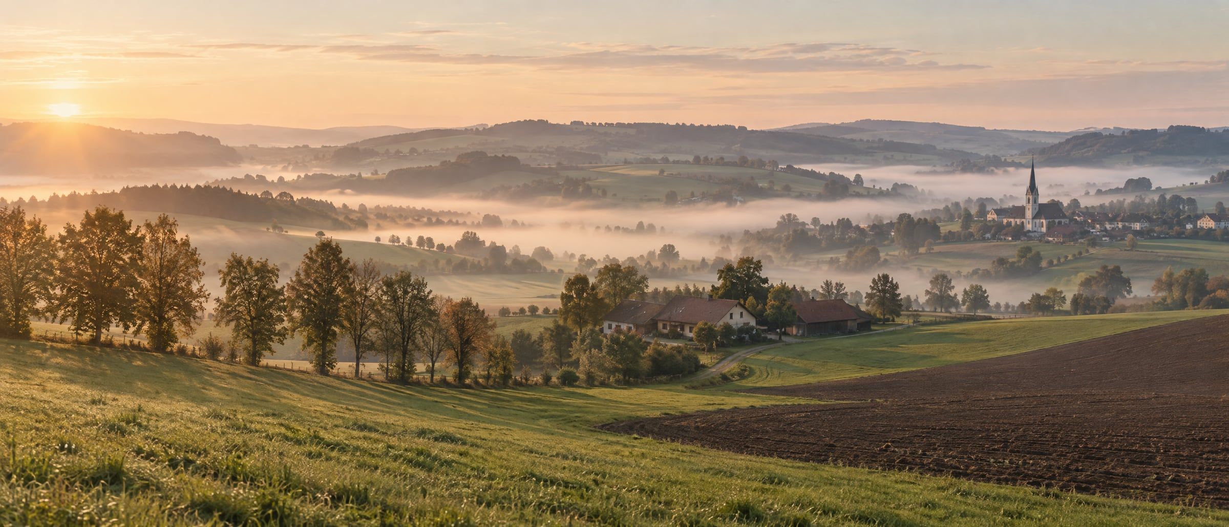 Hügellandschaft am frühen Morgen, Nebel liegt im Tal.